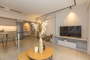 A modern living room with a TV, a round wooden table, and a kitchen in the background. - B Boutique Residences by Raise (Athens)