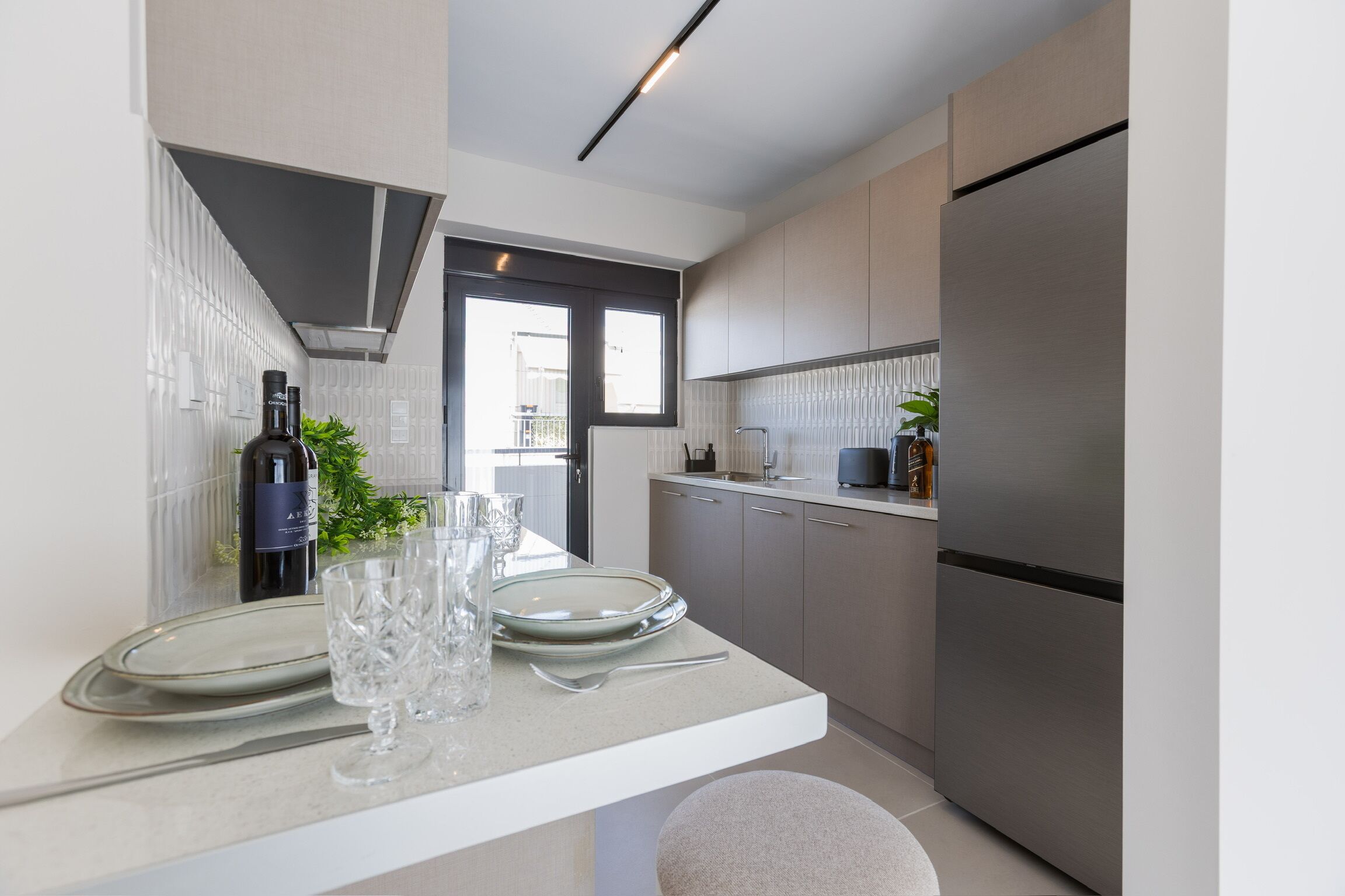 Una cucina moderna con frigorifero integrato, un'area pranzo con tavolo bianco e una finestra che lascia entrare luce naturale.