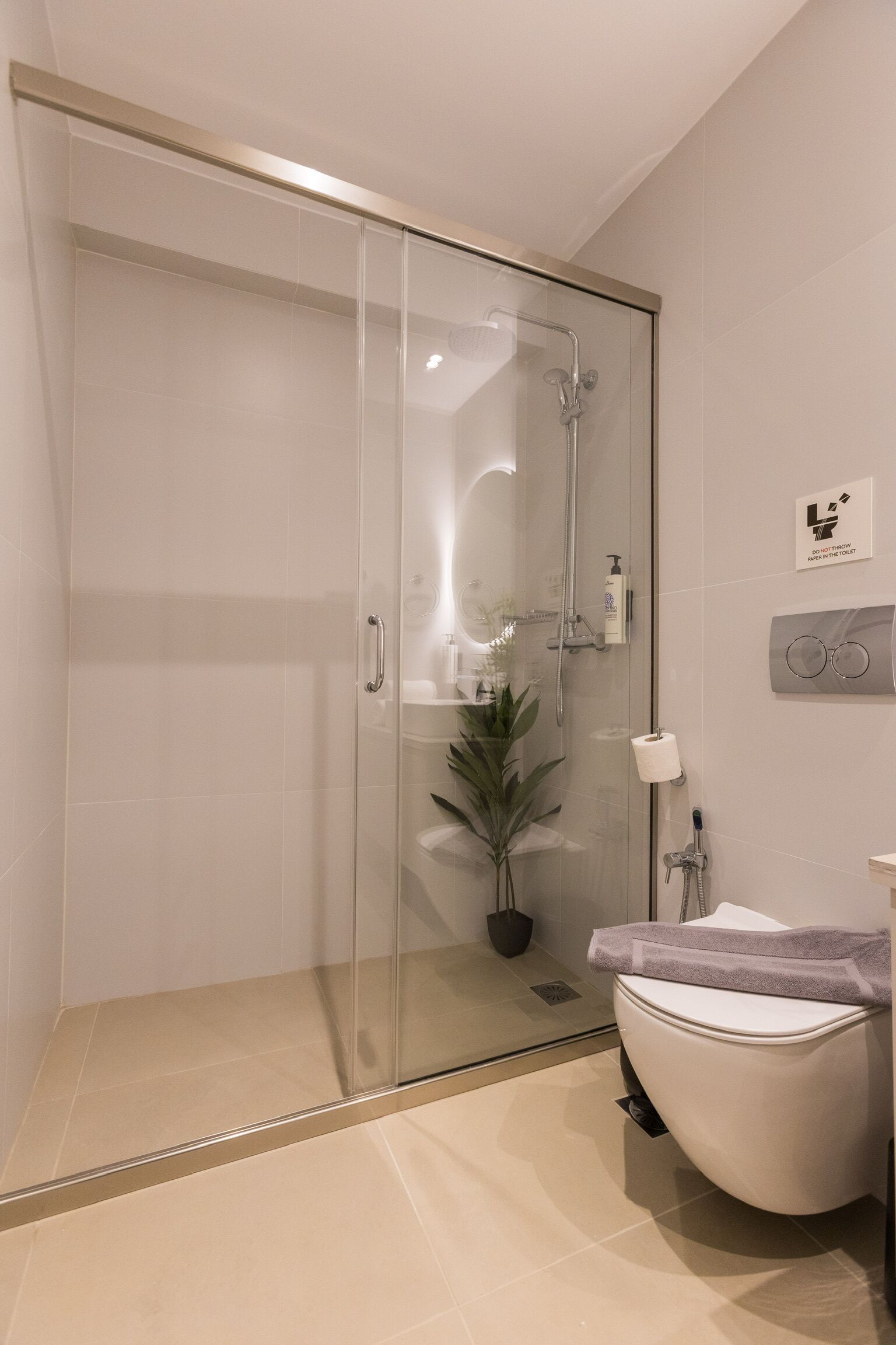 A modern bathroom with a glass-enclosed shower, a toilet, a sink, and a potted plant.