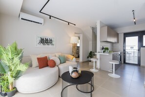 A modern living room with a sofa, a coffee table, and a kitchen area with a bar. - B Boutique Residences by Raise (Athens)