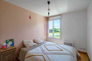 A bedroom with a bed, a nightstand, a window, and a view of greenery outside. - La Perle de Camaret - Belle maison proche du port (Camaret-sur-Mer)