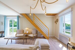 Ein geräumiges Wohnzimmer mit einer Holztreppe, einer Sofagarnitur, einem Couchtisch und Blick ins Freie.