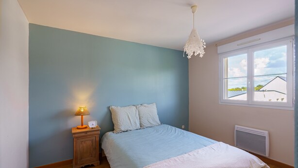 Quarto com cama, mesa de cabeceira com abajur, janela com vista e luminária de teto.