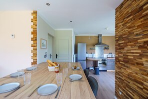 Ein Essbereich mit einem Holztisch, gedeckt für vier Personen, einer Küche im Hintergrund und einer Wand als Holzdekor.
