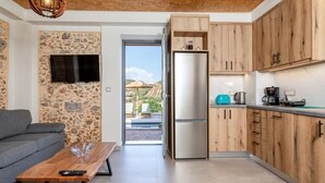 A modern kitchen with wooden cabinets, a built-in fridge, and a dining area with a grey sofa and a wooden coffee table. - Villa Elpida (Chania)