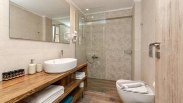 A modern bathroom with a large mirror, a round sink, a shower enclosure, and a toilet.