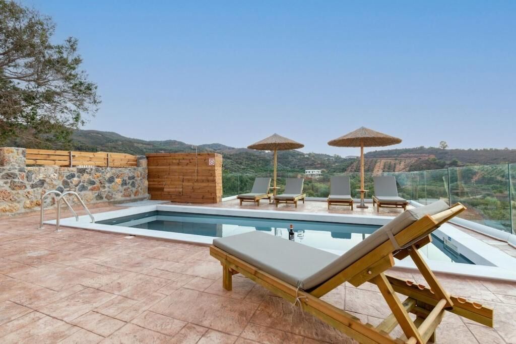 Una piscina infinita al aire libre con sillas de descanso y sombrillas, rodeada de muros de piedra y vistas a las colinas.