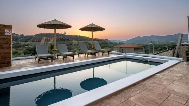 A rooftop infinity pool with lounge chairs and umbrellas, overlooking a hilly landscape. - Villa Elpida (Chania)