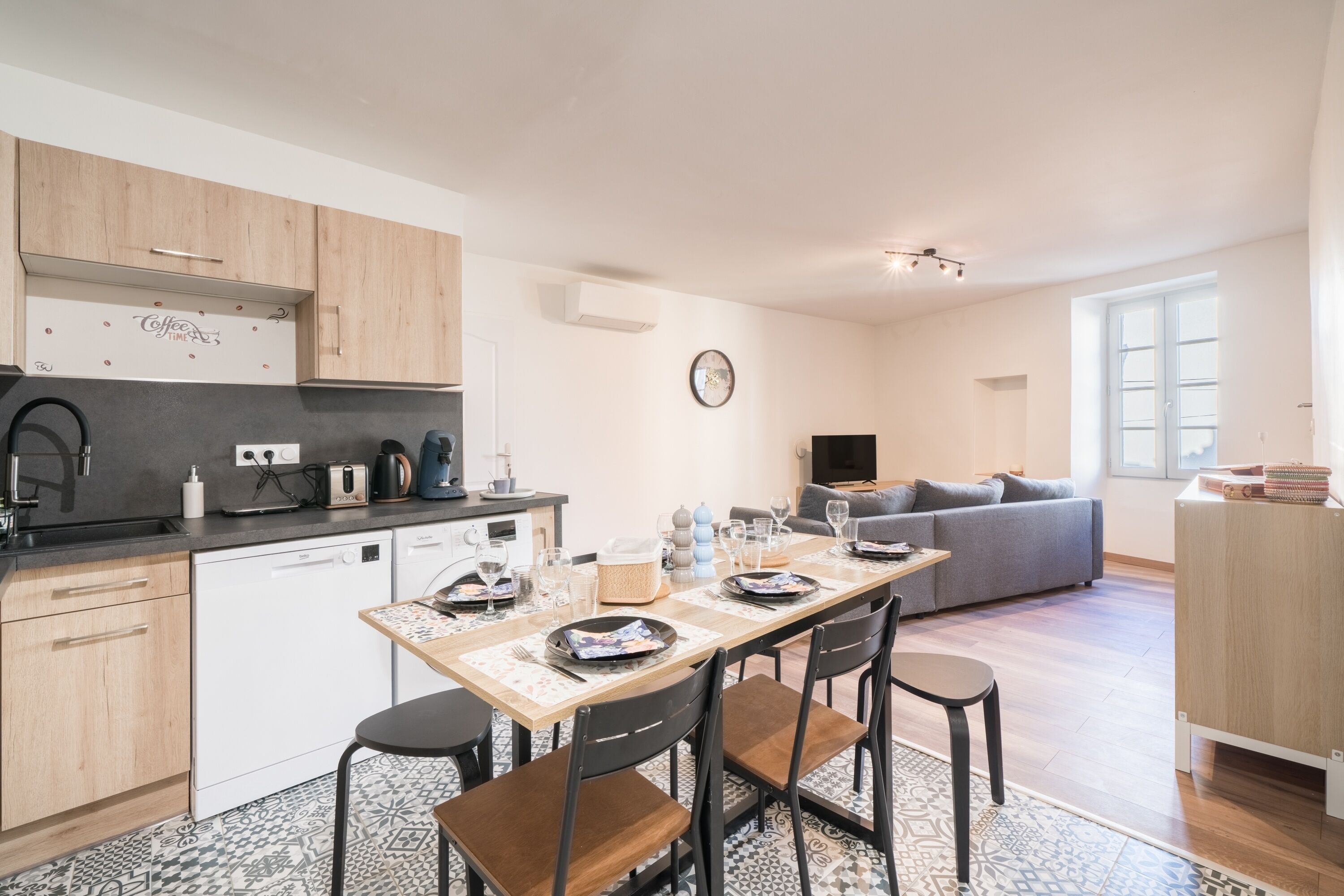 A modern kitchen with a dining area, a sofa, and a TV in a living room.