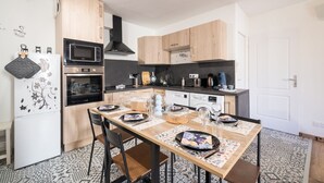 A compact kitchen with wooden cabinets, a microwave, oven, and a dining table set for four. - La Sacristie - Au coeur du village de Donzère (Donzère)