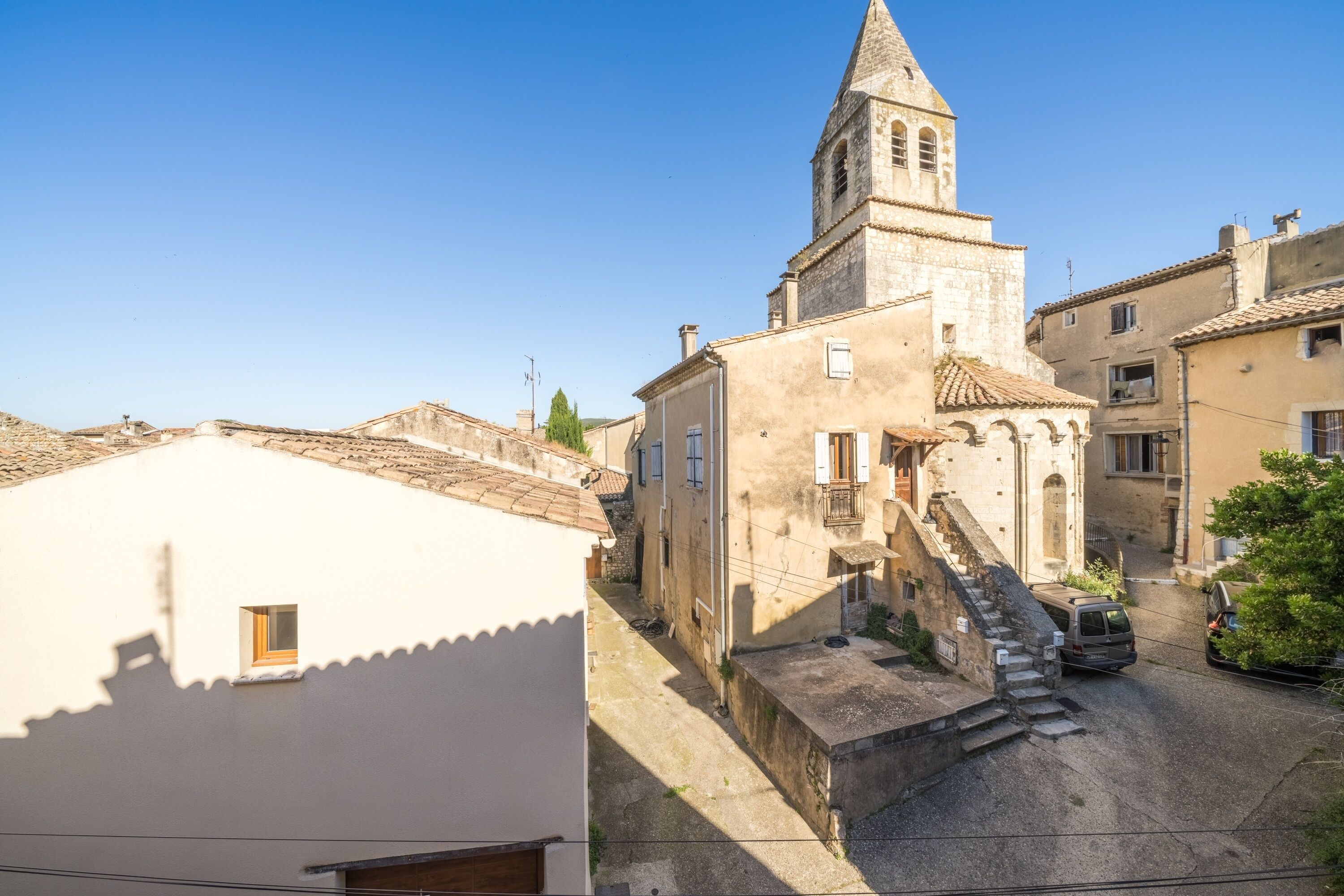 A narrow street with a church tower, a white building with a small window, and a parked car.