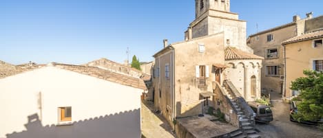 A narrow street with a church tower, a white building with a small window, and a parked car.
