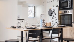 A modern kitchen with a dining table set for four, a microwave, oven, and a refrigerator. - La Sacristie - Au coeur du village de Donzère (Donzère)