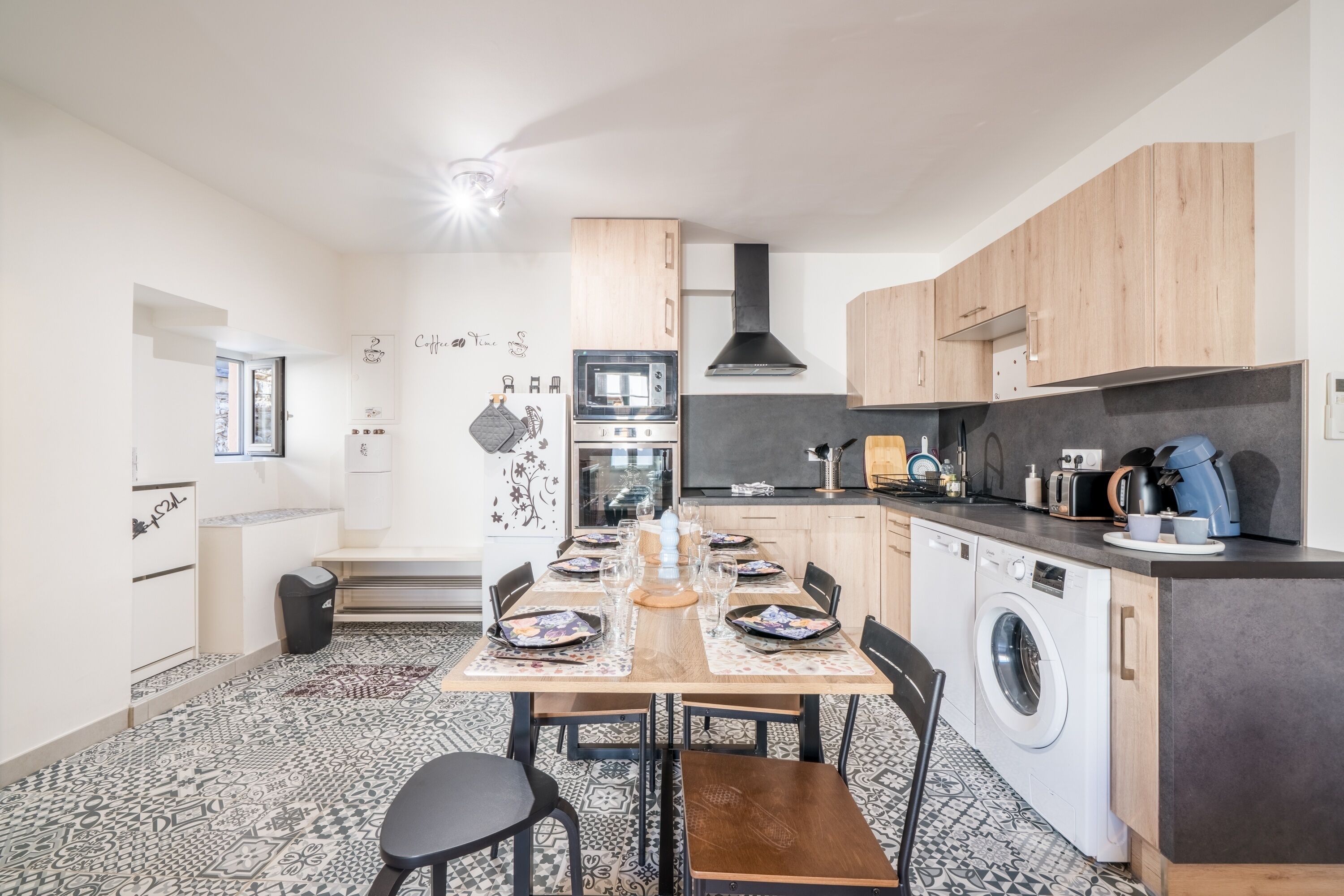 A modern kitchen with a central island, built-in appliances, and a dining area with a patterned floor.
