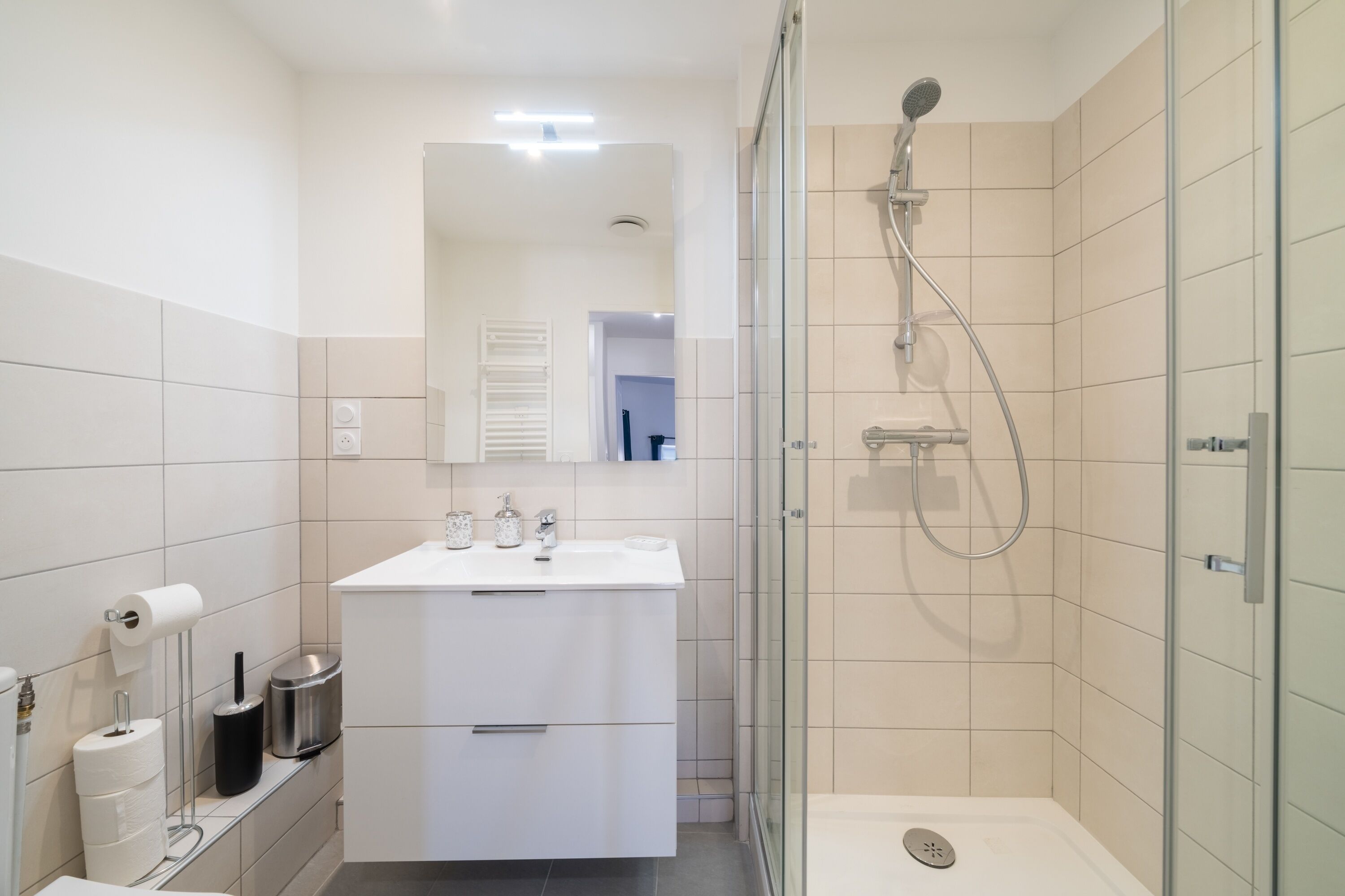 Et moderne badeværelse med bruseniche, hvid kommode og toilet.