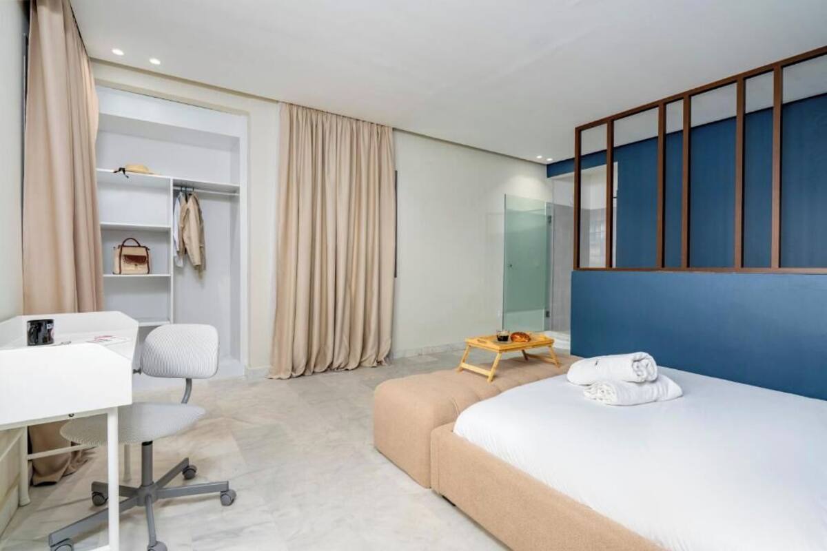 Una habitación de hotel con cama, escritorio, silla, armario y una mesita con bandeja.