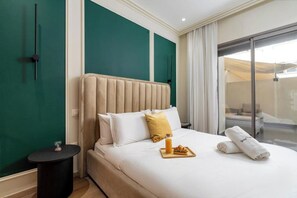 Habitación de hotel con cama, una mesita, una mesita de noche, un ventanal de vidrio que da a un balcón y una pared de acento verde.