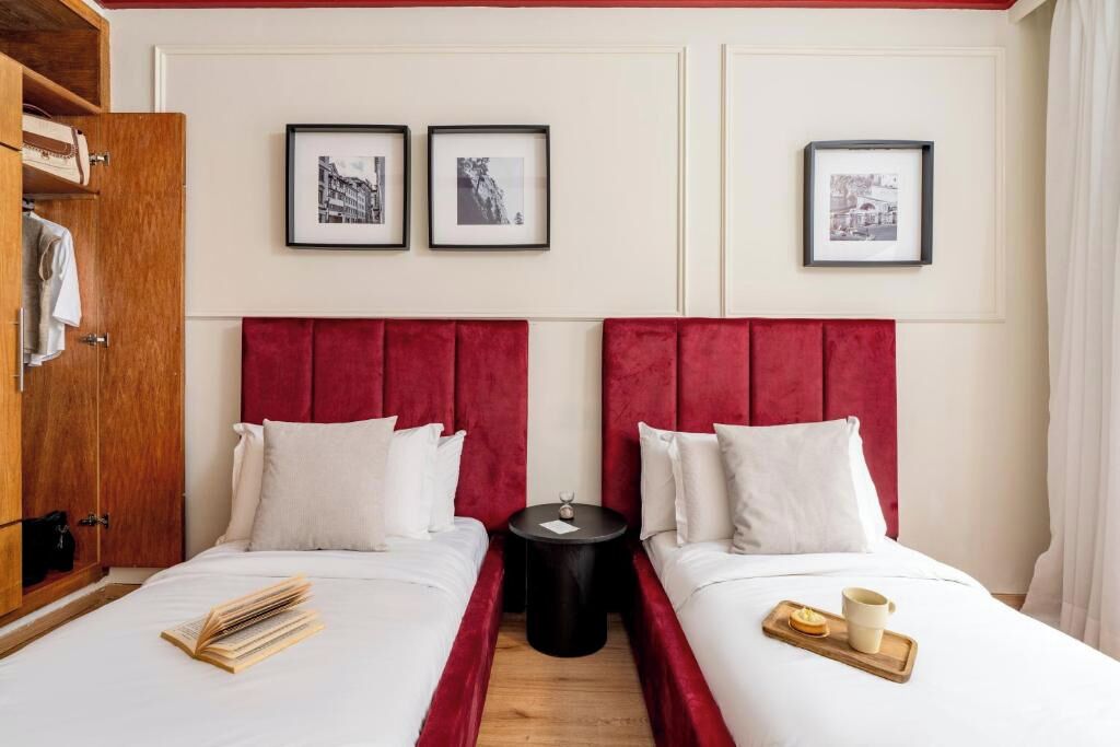 Quarto de hotel com duas camas, um guarda-roupa de madeira e três quadros na parede.
