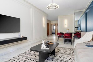 A modern living room with a flat-screen TV, a black coffee table with decorative items, a patterned rug, a red sofa, and a dining area with red chairs. - The Loft  (Casablanca)