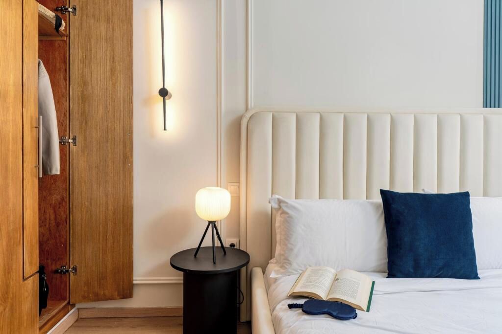 Un dormitorio con cama, mesita de noche con lámpara, armario y aplique de pared.