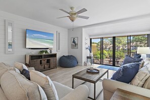 Ein Wohnzimmer mit Fernseher, Sofa, Couchtisch und Blick ins Freie.
