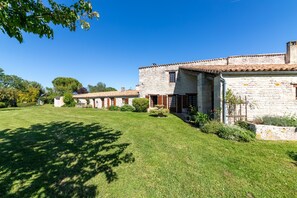Un bâtiment en pierre, surmonté d’un toit de tuiles, entouré d’une pelouse bien entretenue et d’arbres.