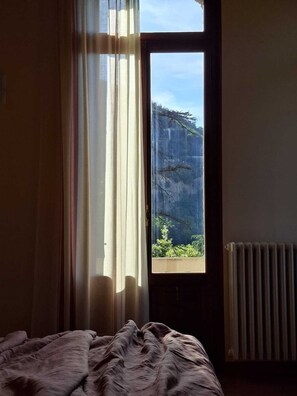 A bedroom with a large window, a radiator, and a bed with a blanket.