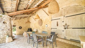 Una habitación de paredes de piedra con techo de madera rústica, suelo de piedra, una mesa con sillas y una cesta grande tejida colgando del techo.