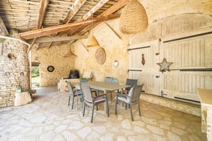 Habitació amb parets de pedra, sostre de fusta rústica, sòl de pedra, taula amb cadires i una forta cistella penjant del sostre.