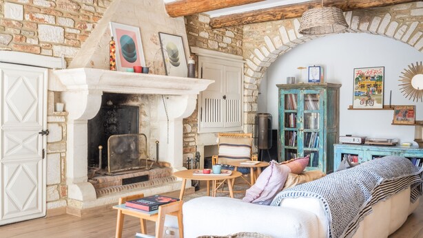 Una habitación rústica con chimenea, un sofá, una estantería y una pared de piedra.