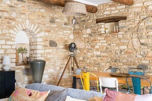 Habitació rústica amb parets de maó descobert, una taula de fusta, un trípode i un gerro gran.