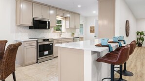 Una cocina moderna con armarios color crema, electrodomésticos de acero inoxidable, una isla central con taburetes y vistas al exterior.