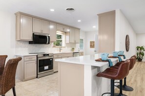 Una cocina moderna con armarios color crema, electrodomésticos de acero inoxidable, una isla central con taburetes y vistas al exterior.