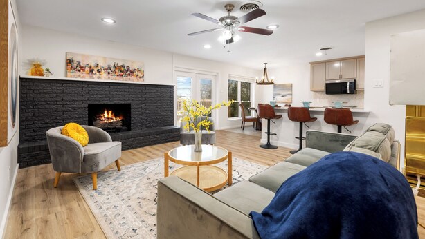 Una sala de estar moderna con chimenea, ventilador de techo y comedor con taburetes de bar.