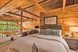 A wooden cabin bedroom with a bed, a map on the wall, a desk with a lamp, and a view of the outdoors. - Wonder View Cabin! (Maggie Valley)