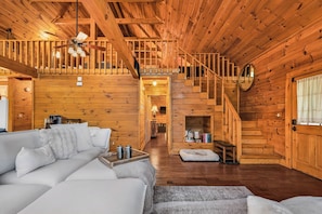 A log cabin interior with a wooden staircase, a living room with a sofa and coffee table, and a fireplace. - Wonder View Cabin! (Maggie Valley)