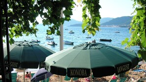 Strandparasoller med 'LANGUST' branding, strandstole og udsigt til både på vandet.