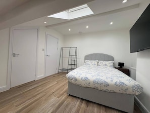 A bedroom with a skylight, a bed with floral bedding, a bedside table, and a TV mounted on the wall. - Central Leeds - House - Stay 6 - Parking - Garden (Leeds)
