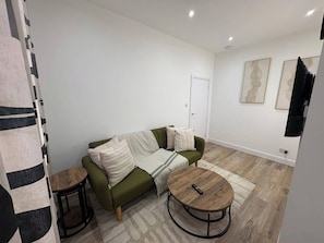 A living room with a green sofa, two round tables, and a door in the background.