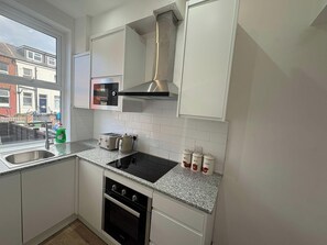 A compact kitchen with white cabinets, a stainless steel range hood, a built-in microwave, a kettle, and a sink. - Central Leeds - House - Stay 6 - Parking - Garden (Leeds)