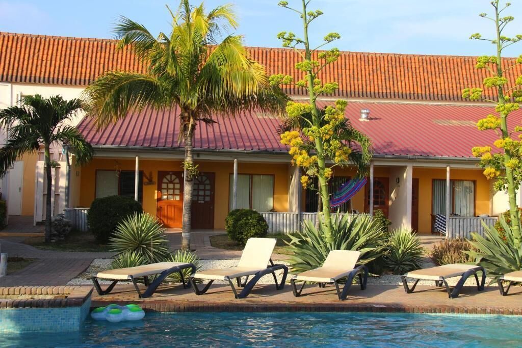 A pool area with lounge chairs, a building with a red roof, and palm trees.