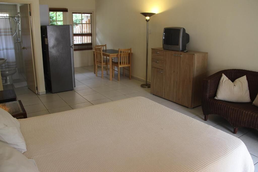 Une chambre d’hôtel comprenant un lit, un téléviseur posé sur un meuble, un coin repas avec des chaises et un espace douche.