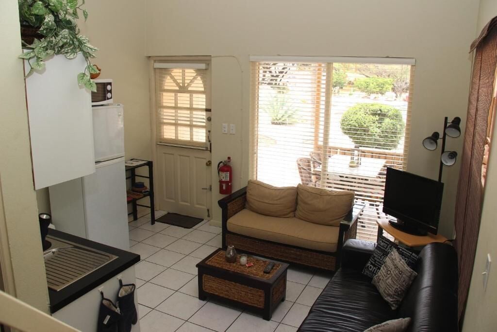 A compact living space with a kitchenette, a sofa, a television, and a window with blinds.