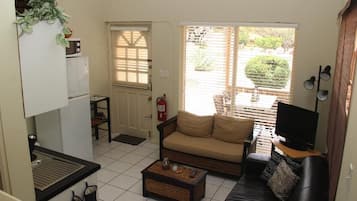 A compact living space with a kitchenette, a sofa, a television, and a window with blinds.