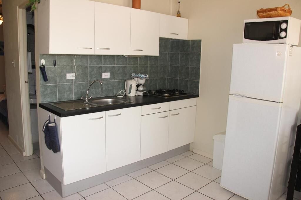 A kitchen with white cabinets, a sink, a stove, a microwave, and a refrigerator.