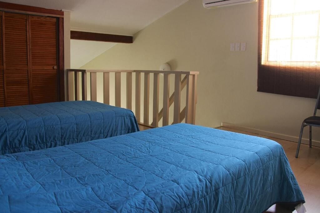 Quarto com duas camas, um guarda-roupa de madeira, janela com persianas e uma cadeira.