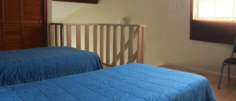 A bedroom with two beds, a wooden closet, a window with blinds, and a chair.