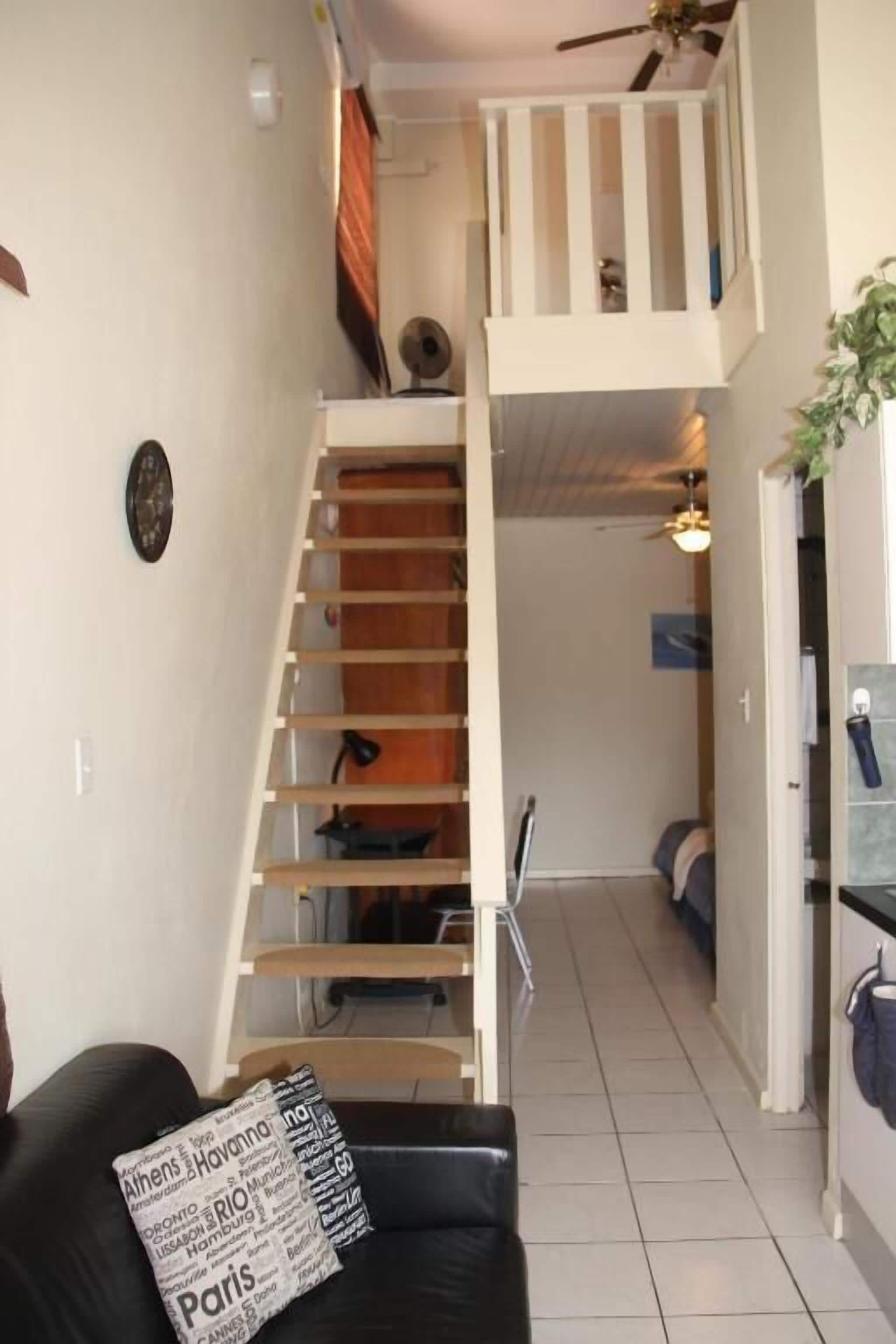 Una habitación con una cama individual, una escalera, un sofá de cuero negro y una mesita pequeña.