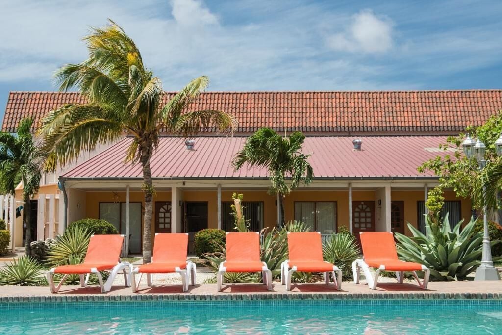 A hotel with a tiled roof, a swimming pool, and orange lounge chairs.