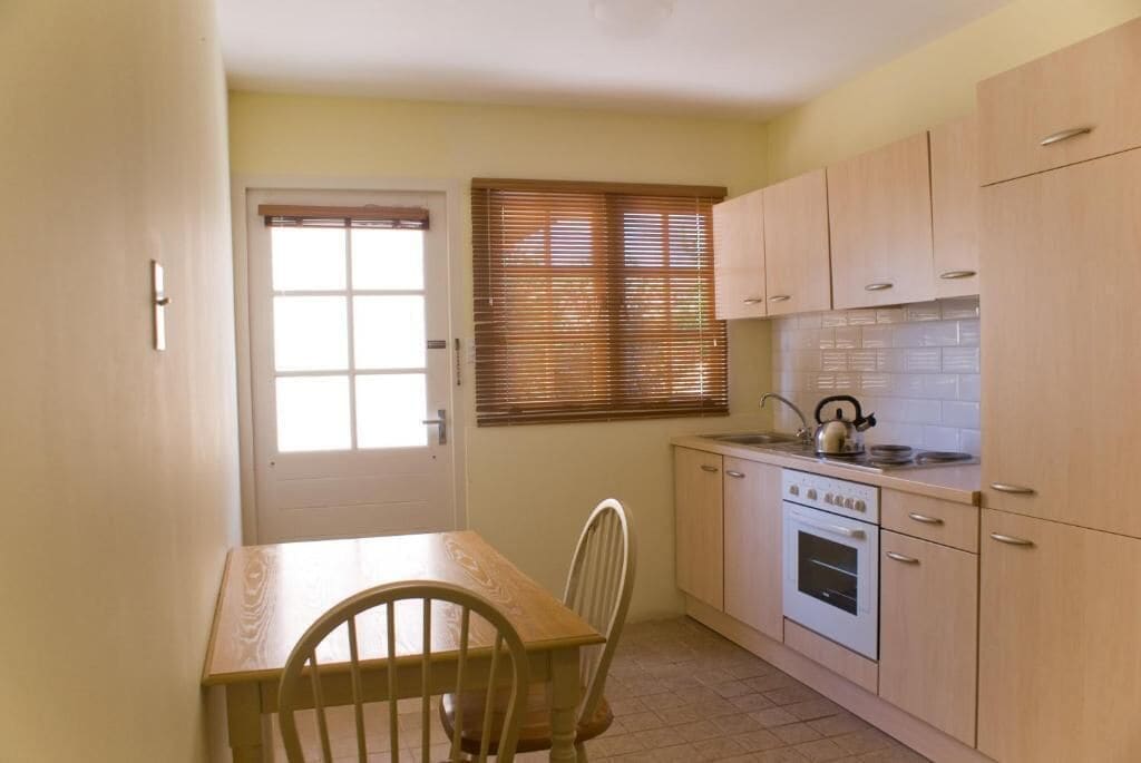 A compact kitchen with a dining table, chairs, a stove, and a window with blinds.